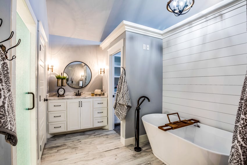 Classic bathroom with tile floors, white walls, gray elements, cabinets, mirror, and bathtub