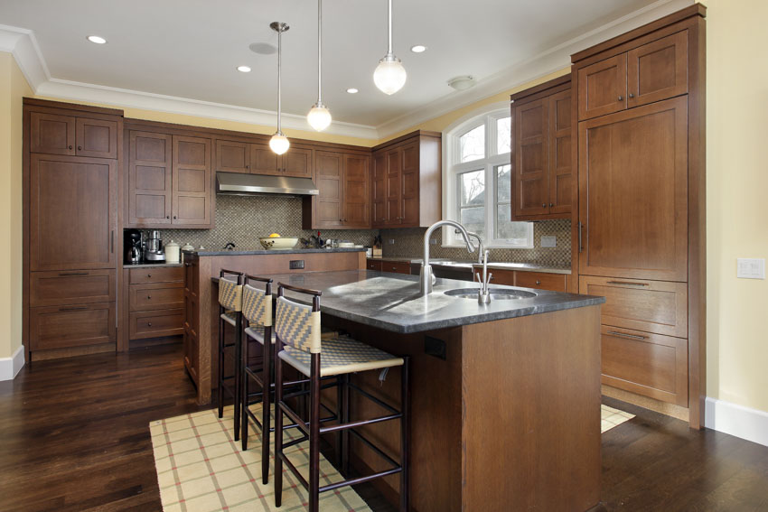 Dark wood cabinets and floors with gray soapstone countertops and beige tile backsplash 