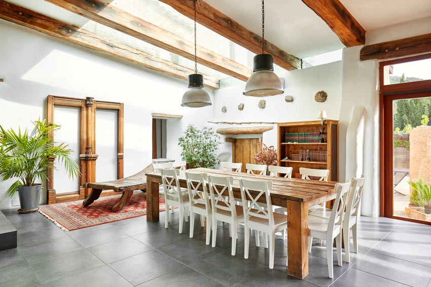 Dining area with tile flooring, wood table, pendant light, door, indoor plant, and exposed ceiling beam