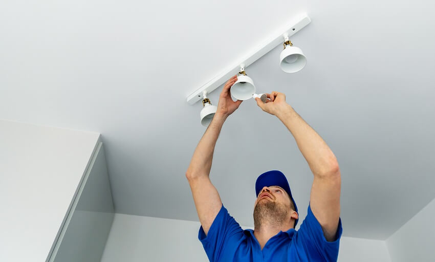 Electrician in blue T-shirt and cap installing LED light bulbs to a white track lighting