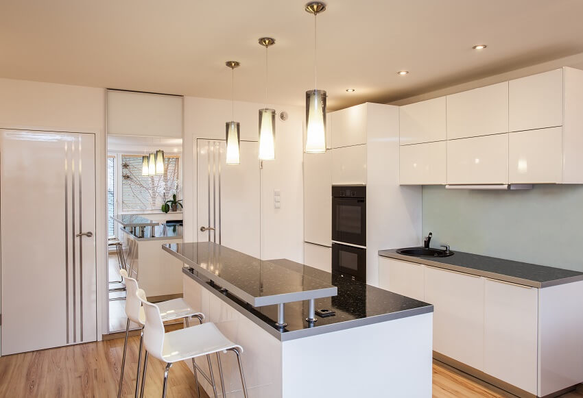 Empty bright kitchen of a flat with mirror wood floors white cabinets black granite countertops and an island with three pendant lights hanging above and white chairs
