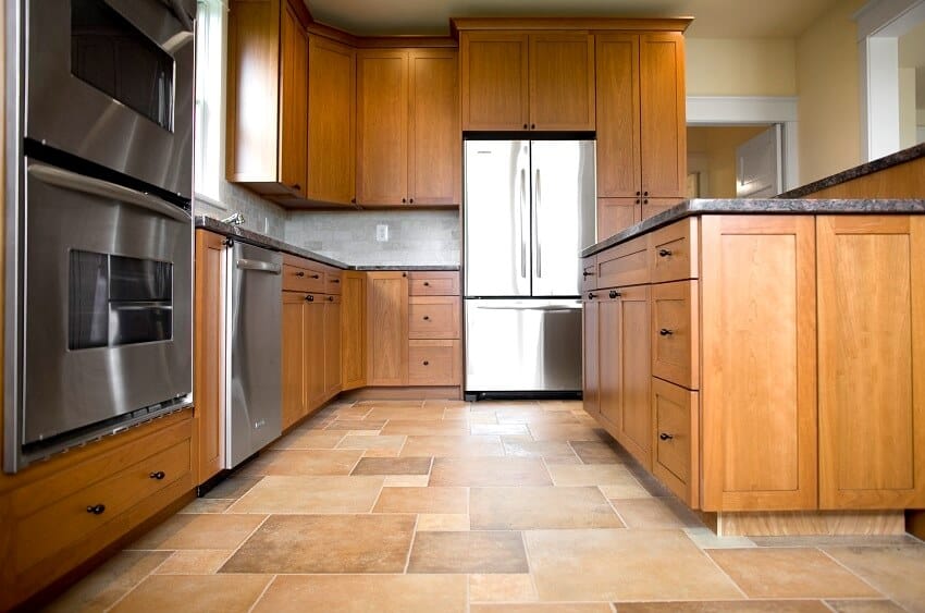 Empty kitchen with wood cabinets stainless steel appliance brick tile backsplash and slate tile floor