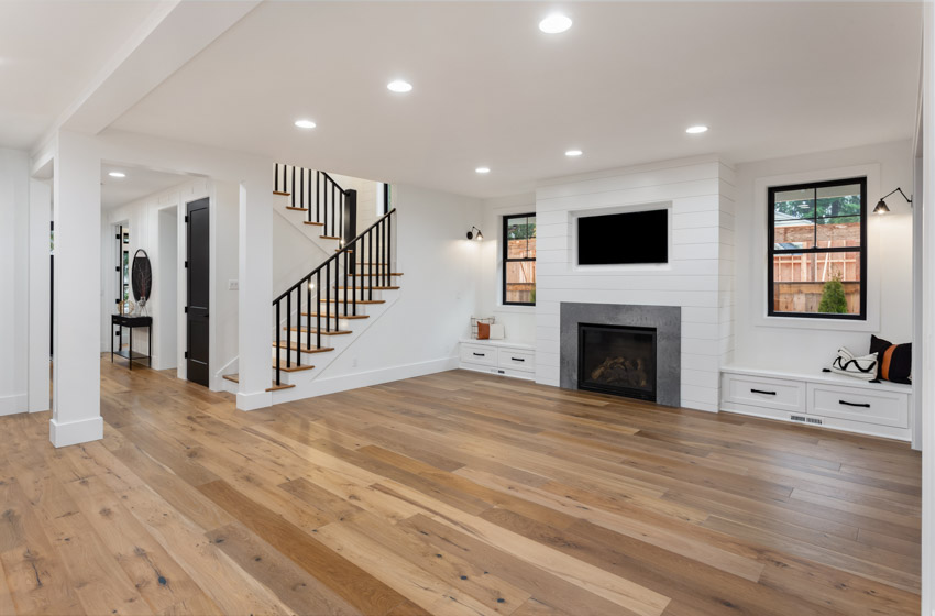 Empty living room with recessed lights, wood floor, fireplace, staircase, and windows