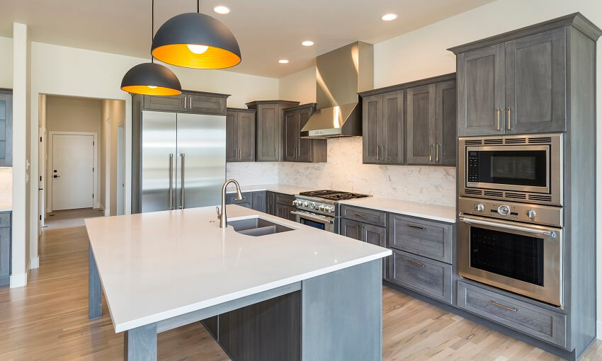 Empty modern farm house kitchen with hardwood floors grey cabinets microwave drawer and pendant lights above island with white countertops and sink