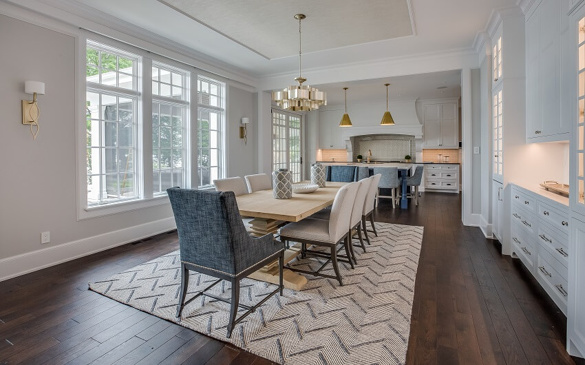 Extended dining area with dark hardwood floors light wood dining table pendant lights white cabinets windows patterned rug view of the kitchen and grey walls