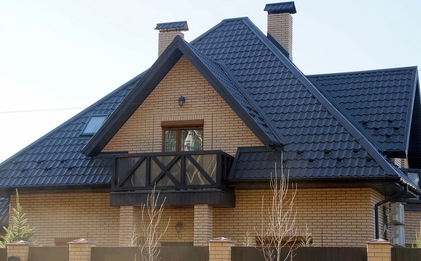 Facade of a brown brick house with a wood balcony windows grey tiled roof and two chimneys with weather resistant chimney cap