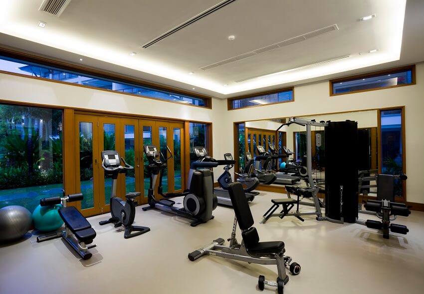 Fitness gym with white interiors a large mirror wood frame glass doors clerestory windows gym equipment LED lights and view of a garden