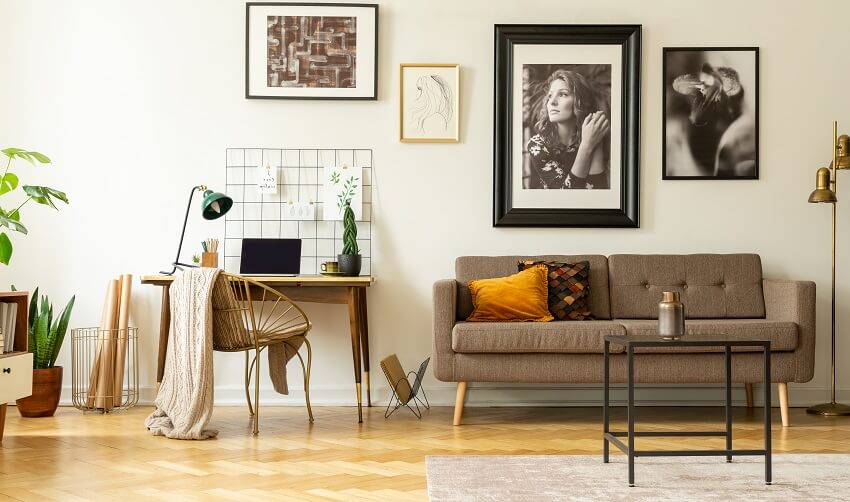 Framed photos gallery on a white wall of a living room with wooden desk, sofa and gold floor lamp
