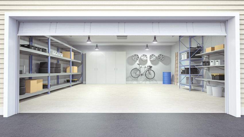 Garage with ceiling lights, door, white siding, sealed floor, and open shelves 