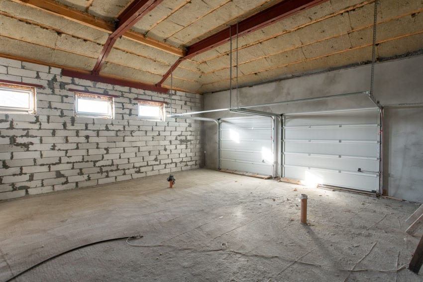 Garage under construction with exposed ceiling insulation, concrete floor, tracked doors, and windows