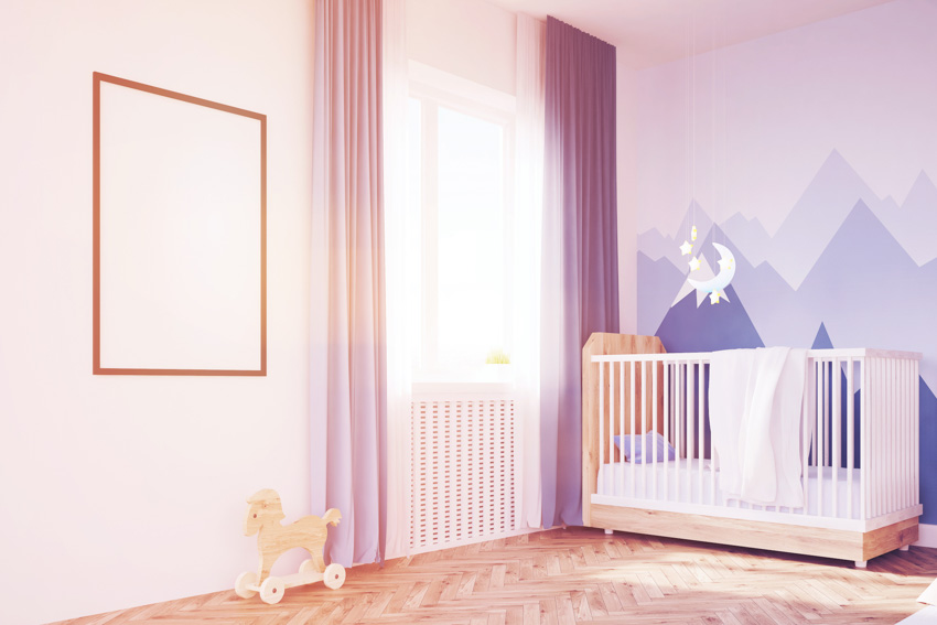 Girls nursery room with accent wall, crib, wood floor, and window curtain
