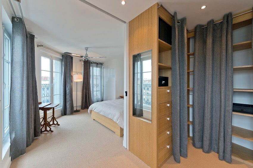 Guest bedroom with white walls wood shelves and cabinets carpeted floors grey curtains wood furniture and a ceiling fan