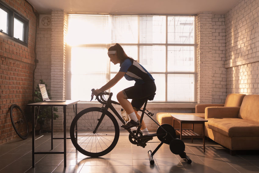 Home office employee working out on an exercise bike in a room with brick walls, couches, and laptop