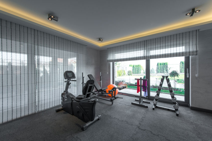 Home office gym with window curtains, tray ceiling, fitness equipment, and gray flooring