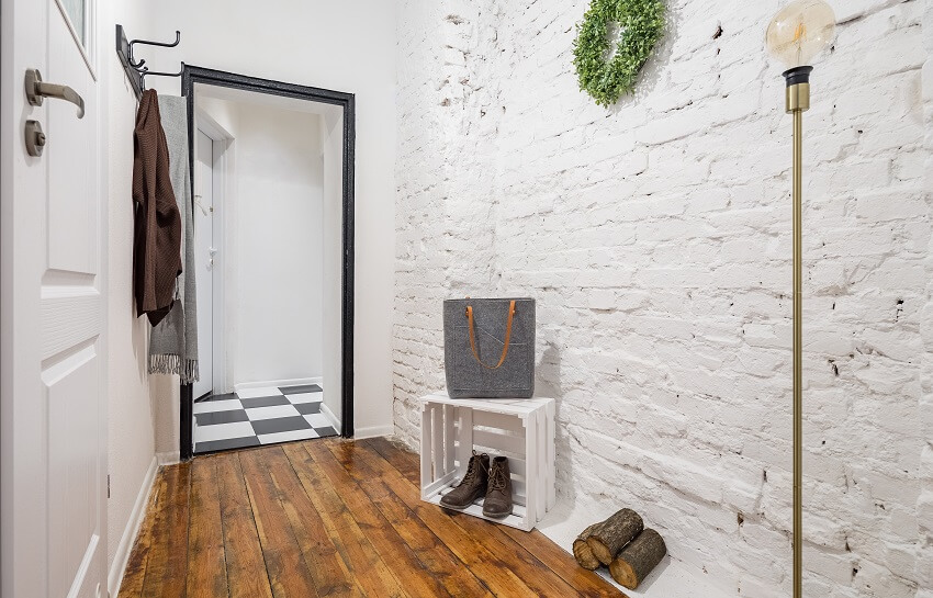 Industrial style mudroom with white brick wall rustic hardwood flooring coat hooks and a lamp