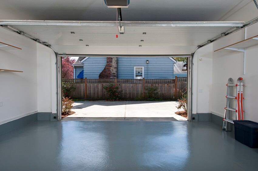 Interior of an insulated garage with grey floors open shelves foldable ladder and a single garage door