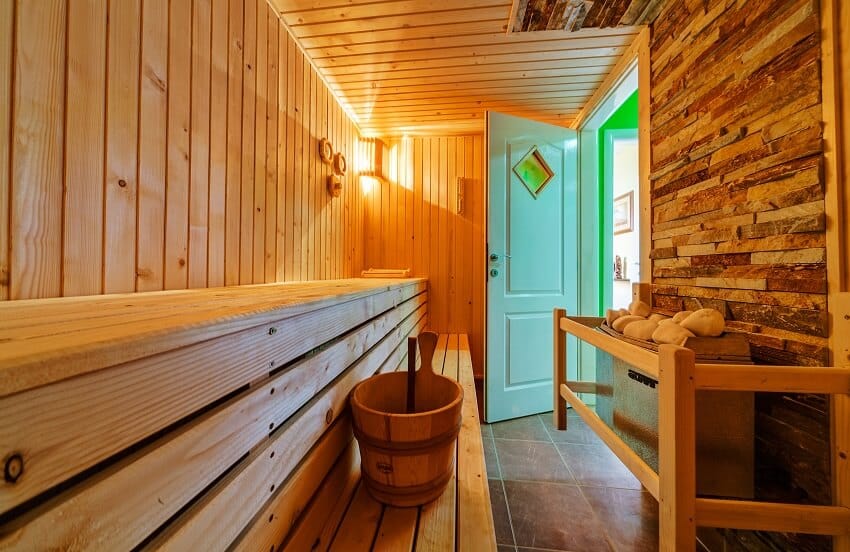Interior of a small wooden home sauna with lighting fixtures and stone wall