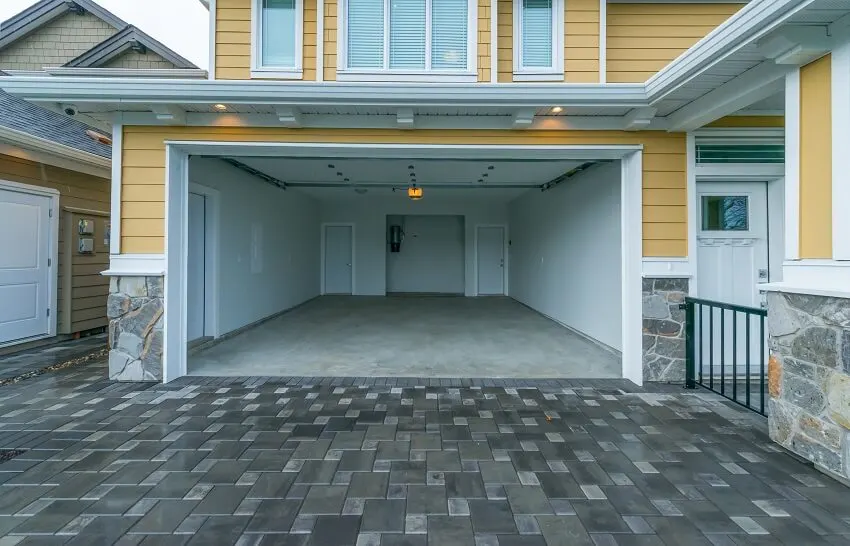 Interior of the empty garage with lighting fixtures and concrete floors in a residential house with yellow facade and grey slate tile driveway