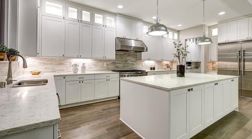 White shaker cabinets, stone-like subway tile backsplash, hardwood floors and pendant lights
