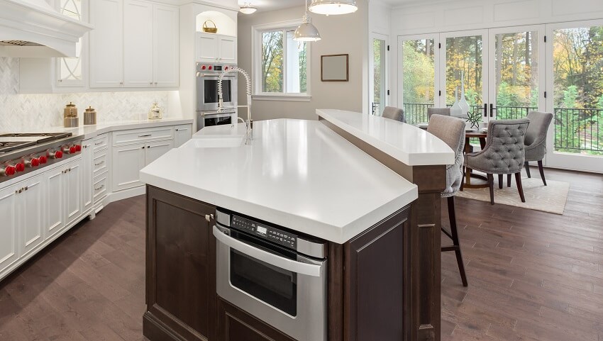 Kitchen in new luxury home with hardwood floors pendant lights island with white countertops and microwave drawer white cabinets range with red knobs and grey dining chairs