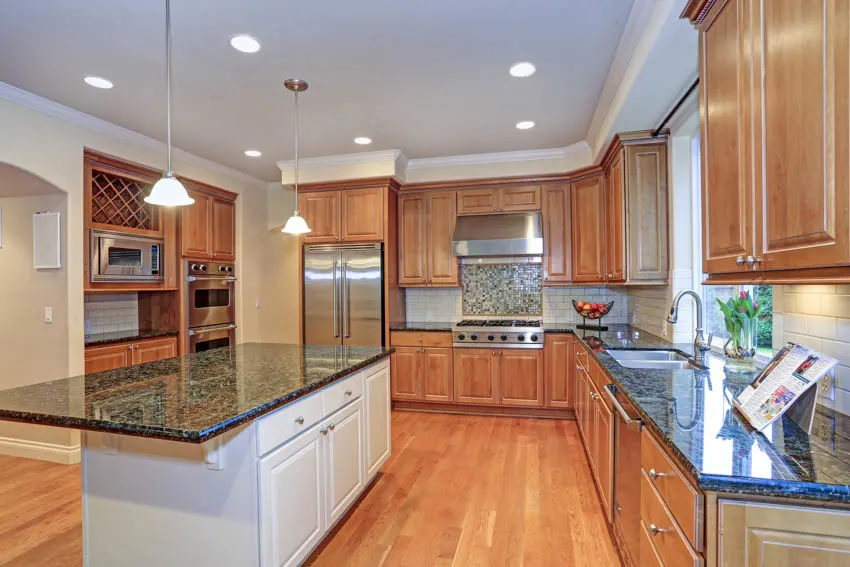 Kitchen space with pendant light, center island, labradorite countertop, wood cabinets, floor, and backsplash