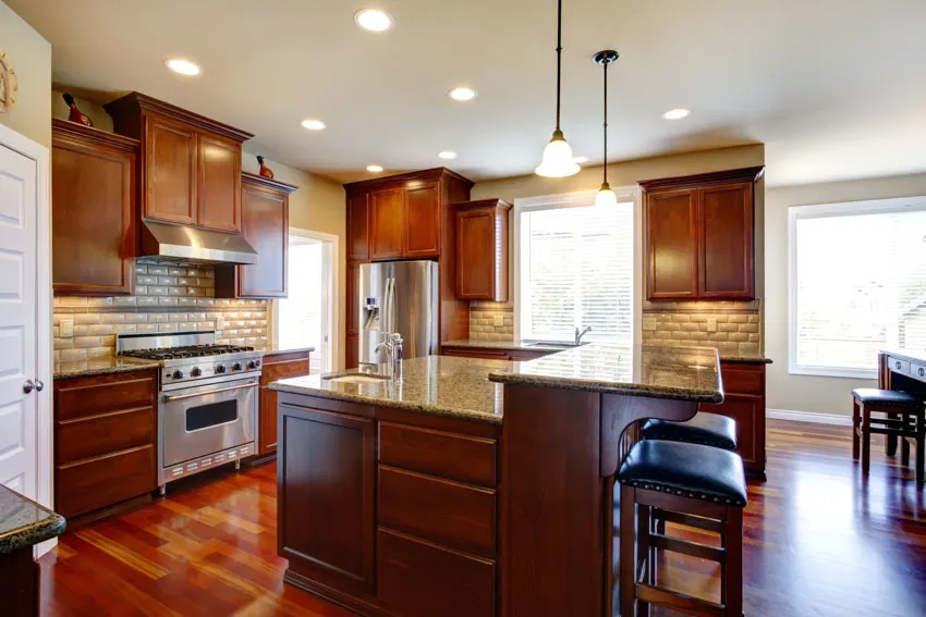 Kitchen space with red oak cabinets, center island, pendant lights, wood flooring, range hood, and tiled backsplash