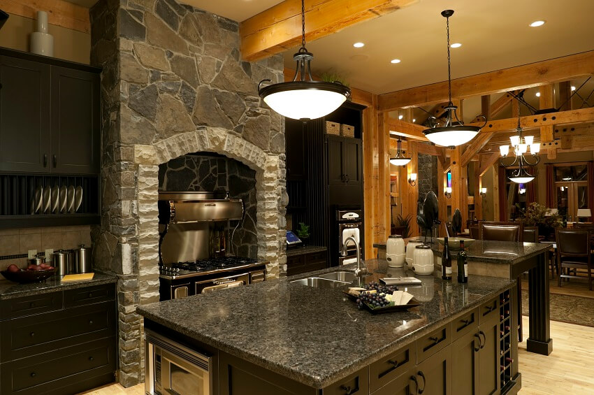 Kitchen with black cabinets and countertops pendant lights island cook range fitted in a stone wall and view of the dining area with post and beams