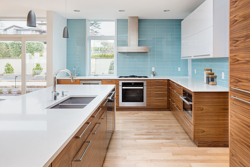 Kitchen with blue tile backsplash as accent wall, range hood, cabinets, oven, center island, and wood flooring