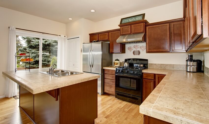 Kitchen with ceramic tile countertops wood cabinets and floors windows with white curtain and island with sink