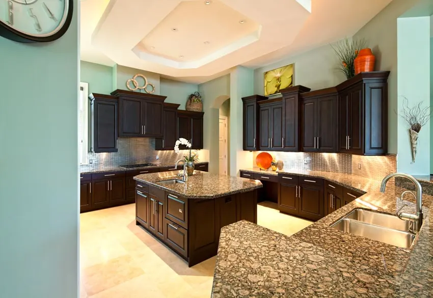 Kitchen with gemstone countertop, green wall, dark wood cabinets, center island, and sink