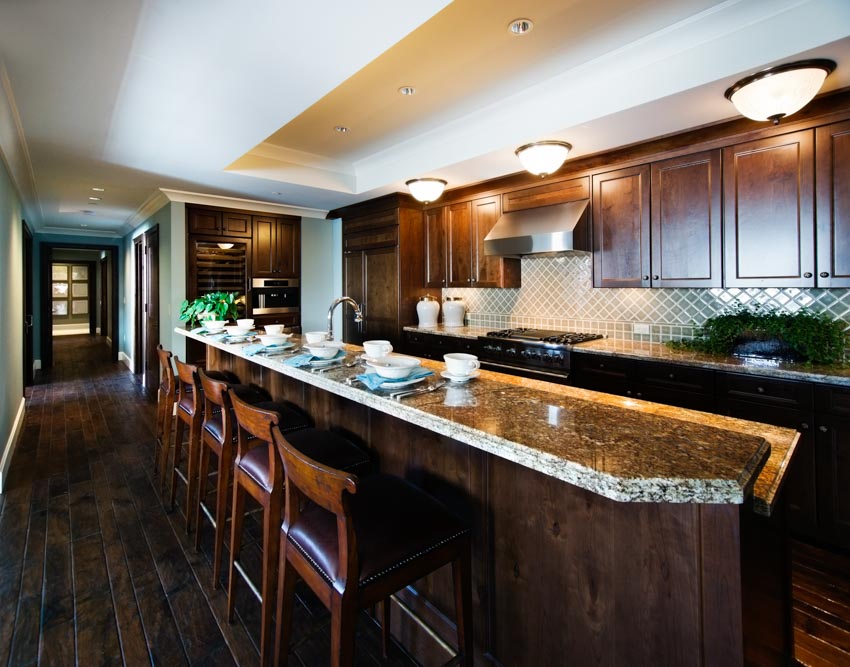 Kitchen with gemstone countertop on island, chairs, lighting fixtures, wood floor, and cabinets