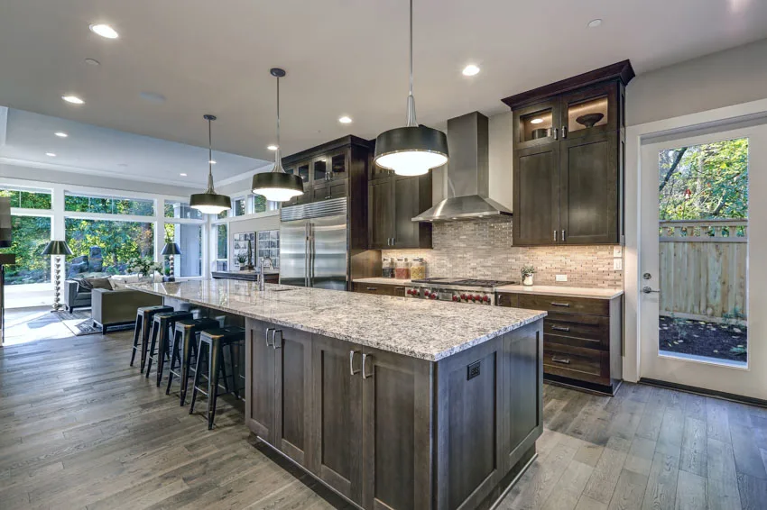 Kitchen with granite countertop, pendant light, wood floor, dining space, windows, glass door, range hood, and backsplash