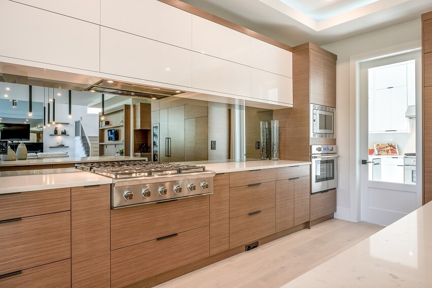 Kitchen with mirror backsplash, large cooktop and handleless cabinets