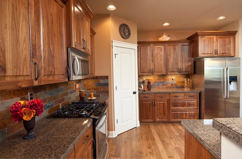 Kitchen with granite tile countertops, stained cabinets, stainless steel appliances and a slate backsplash