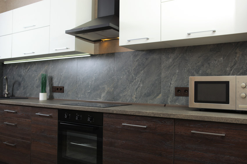 Kitchen with gray soapstone backsplash, cabinets, and range hood