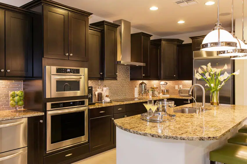 Kitchen with dark brown cabinets, island with rounded corners and glass tile backsplash