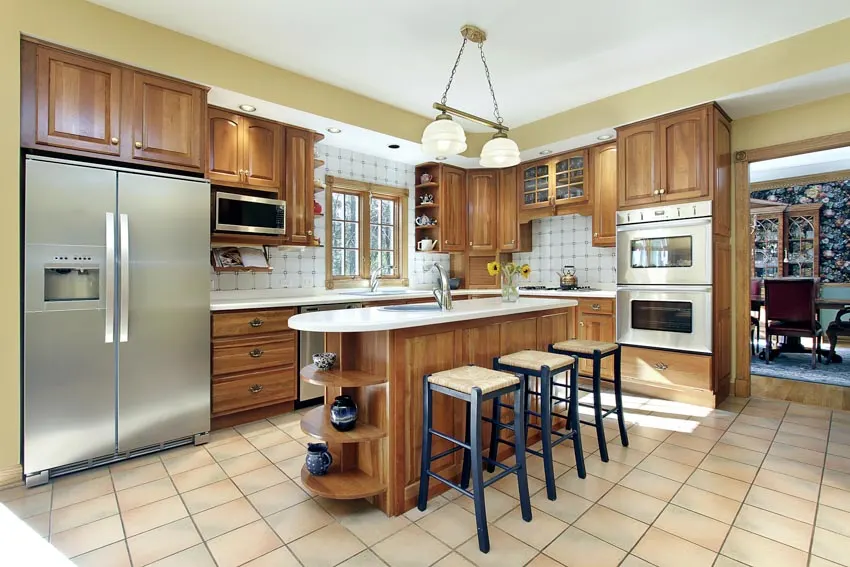 Kitchen with tile flooring, wood-cabinetry, center island, stools, countertop, and appliances