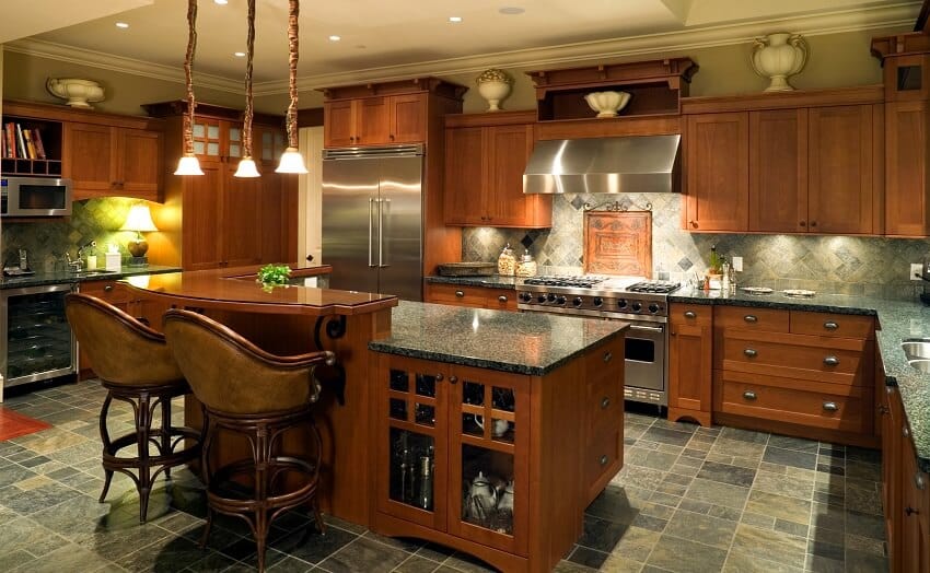 Kitchen with wood cabinets granite countertops grey tile backsplash slate tile floor pendant lights and an island with wood breakfast counter and stools with arm rest