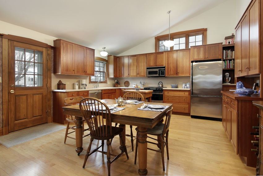 Kitchen with wood flooring, oak cabinets, table, chair, backsplash, and door
