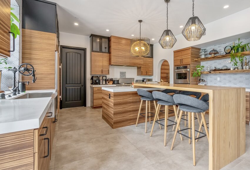 Large kitchen with bamboo cabinets wood breakfast counter with barstools pendant lights large ceramic tile floor white countertops and wood open shelves with decors