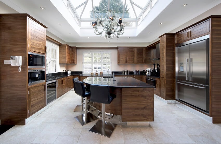 Large kitchen with dark walnut cabinets slate floor curved design kitchen island with three black leather stools and a large skylight window