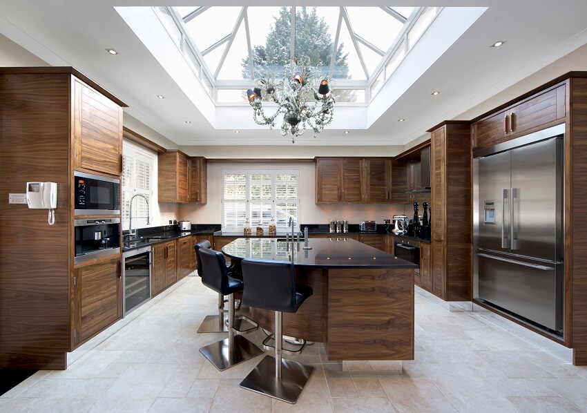 Large kitchen with stainless steel appliance dark wood cabinets large skylight window and a curved island with black granite countertops and barstools