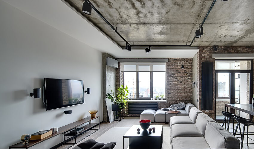 Living room in a loft style with white and brick walls concrete ceiling with track lighting grey sofa wooden tables armchair and carpet on parquet floor