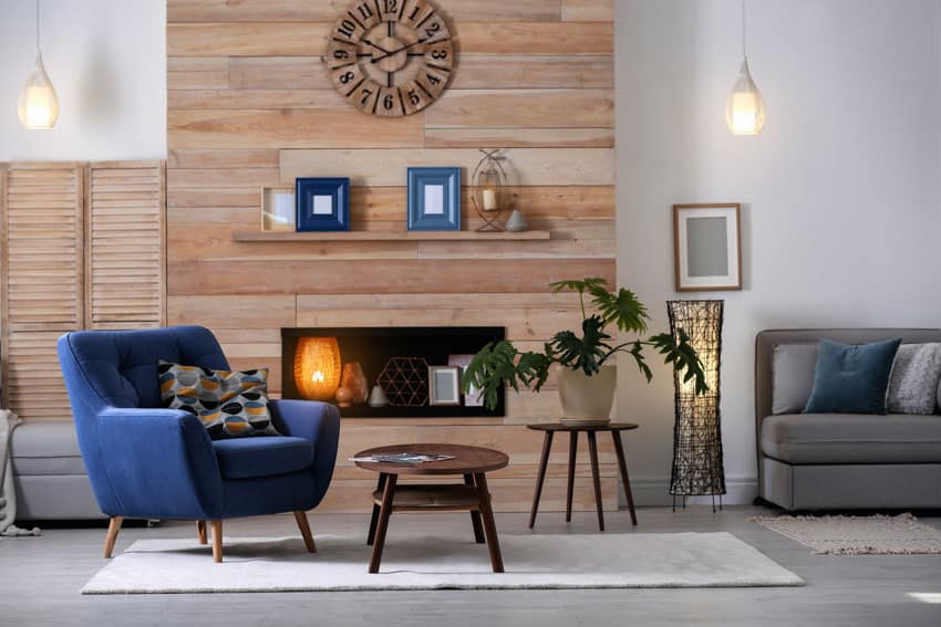 Living room with accent wall, blue chair, couch, hanging light, and fireplace
