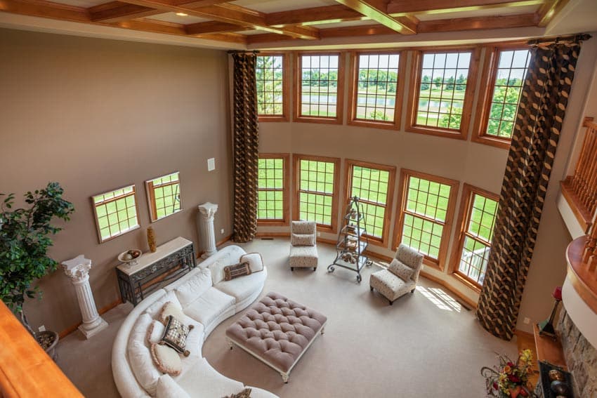 Living room with tall ceiling made of wood, windows, couches, chairs, and carpeted floor