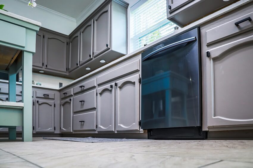 Low angle view of a renovated kitchen in an older home with painted gray cabinets marble countertops a small portable island and a tiled floor