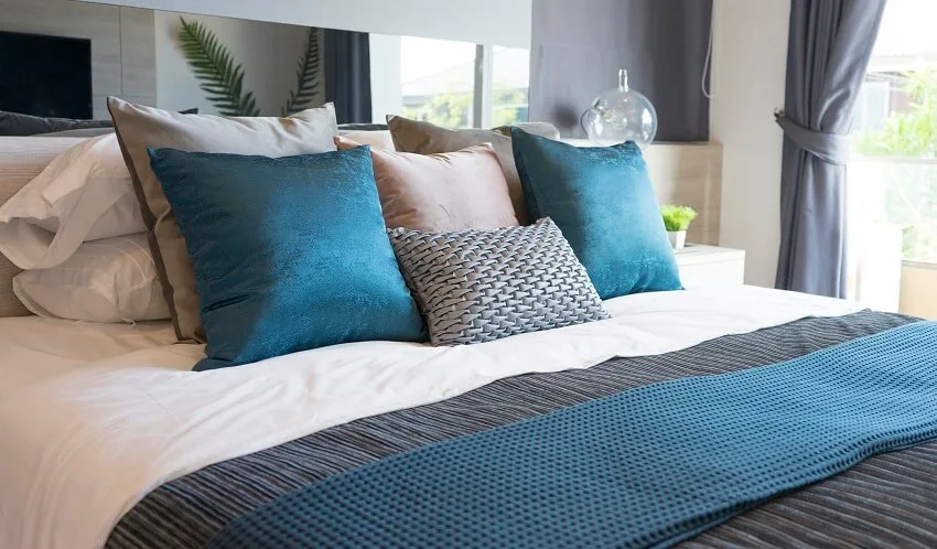 Luxury set of blue and gray pillows on bed with mirror behind headboard