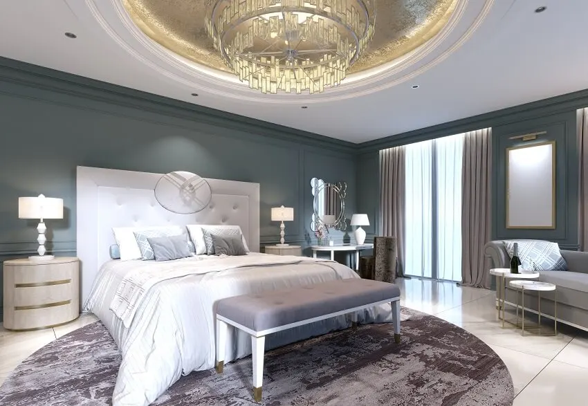 Mansion bedroom with large comfortable bed sofa bench coffee tables dark grey walls round carpet on marble tile floors and an elegant chandelier