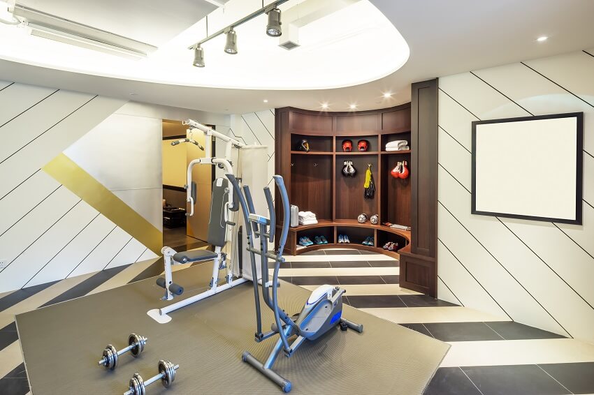 Modern home gym with tile floor panel wall dark wood cubby storage with bench lighting fixtures and gym equipment on grey mat