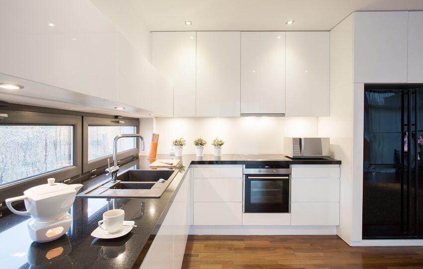 Modern kitchen with black fridge, and white cupborads with under lighting 